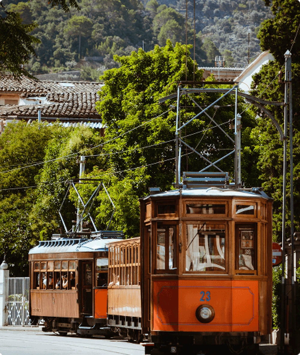 Iconic vintage wooden tram passing through the historic town of Sóller, surrounded by lush greenery and mountain views