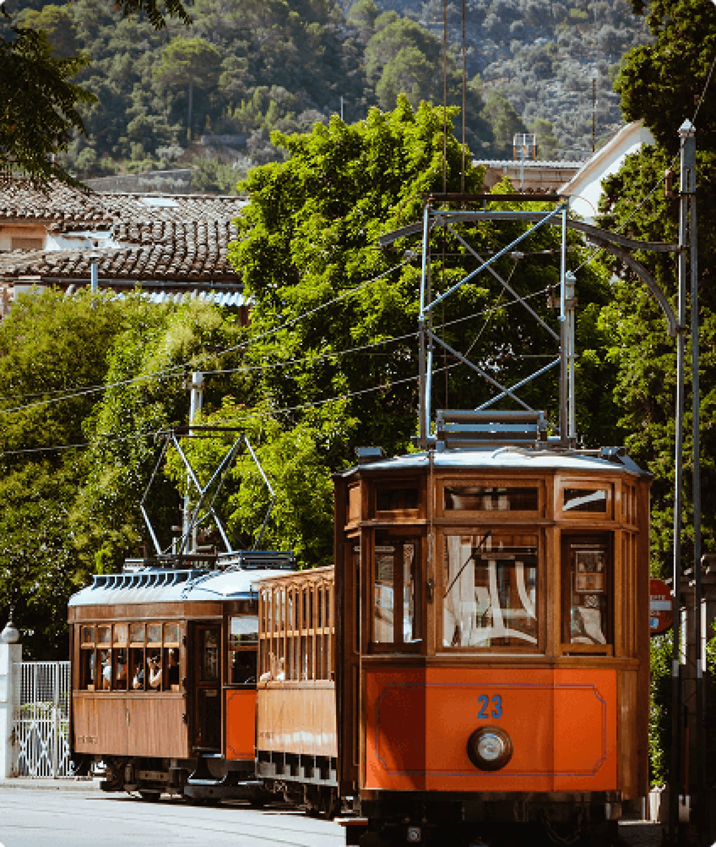 Iconic vintage wooden tram passing through the historic town of Sóller, surrounded by lush greenery and mountain views